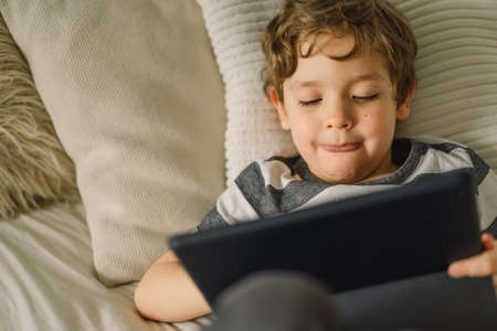 Little Boy with a tablet in the room. The boy play game on the tablet. Technology concept. Child with a gadgetの写真素材