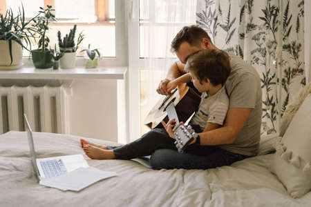 Father and son learn to play the acoustic guitar in an online lesson. Free time to spend with my son...