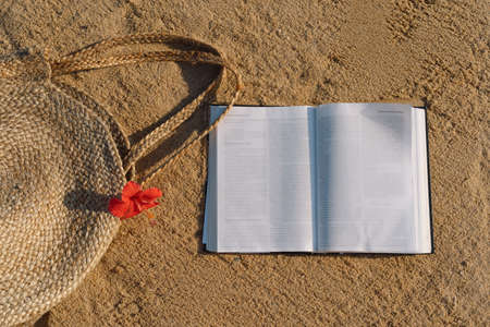 Summer vacation still life. Straw bag, flower and open book. Summer time. Holiday by the sea....