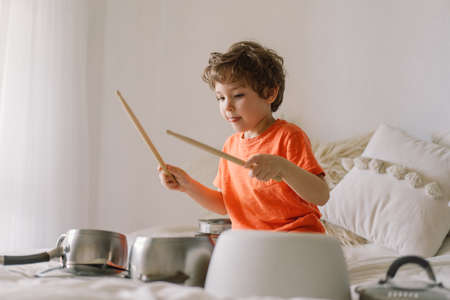 Cute young boy using wooden sticks to bang saucepans that are set up like a drumset. Quarantine timeの写真素材