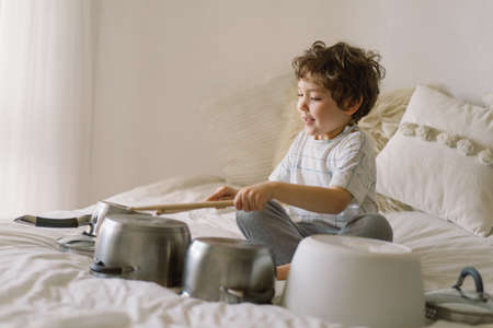Cute young boy using wooden sticks to bang saucepans that are set up like a drumset. Quarantine timeの写真素材