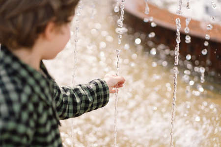 Curly boy playing at the fountain. Little boy plays in the square between the waterの写真素材