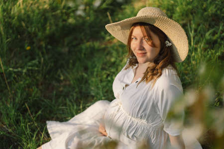 Spring portrait of a pregnant woman. A beautiful young pregnant woman in a white dress walks in the spring garden. Happy pregnancy. Springの写真素材