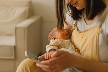 Mother sitting on bed and typing on the cellphone while son is napping. Focus on baby