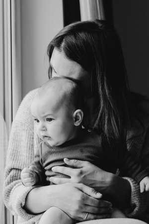 Mother playing with baby son at home near the window. Happy infant and mom. Isolation during quarantine on Mother's dayの写真素材