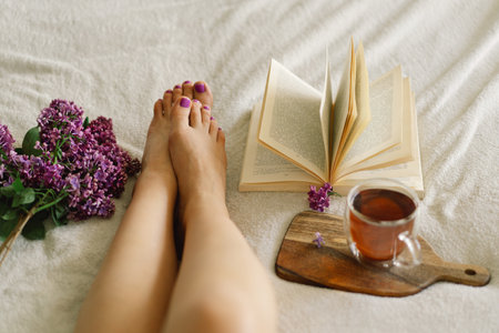 Female feet with purple pedicure, book and lilac. Cozy leisure scene. Woman relaxingの写真素材