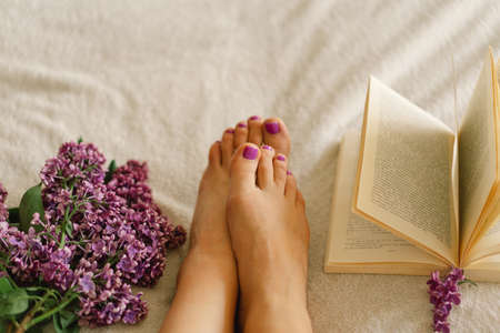 Female feet with purple pedicure, book and lilac.