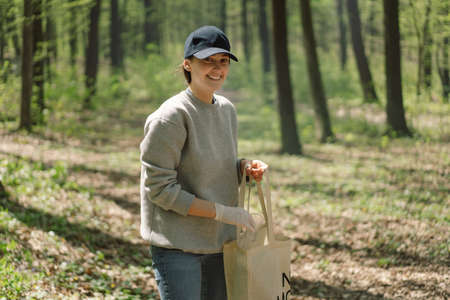Volunteer woman is cleansed in the forest. Woman collects plastic. Woman volunteer with a bag with...