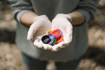 Woman hands are holding a handful of multi-colored plastic lids. Concept of environmental pollution, eco friendly behavior, waste sorting and plastic recycling.の写真素材