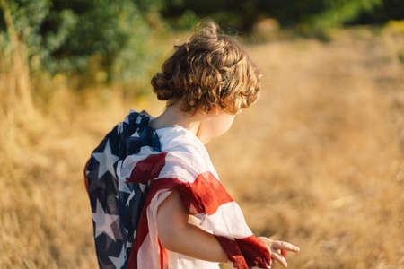 Happy little boy patriot running in the field with American flag. USA celebrate 4th of Julyの写真素材