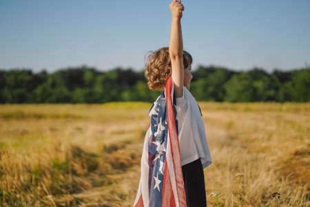 Happy little boy patriot running in the field with American flag. USA celebrate 4th of Julyの写真素材