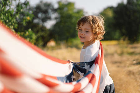 Happy little boy patriot running in the field with American flag. USA celebrate 4th of Julyの写真素材
