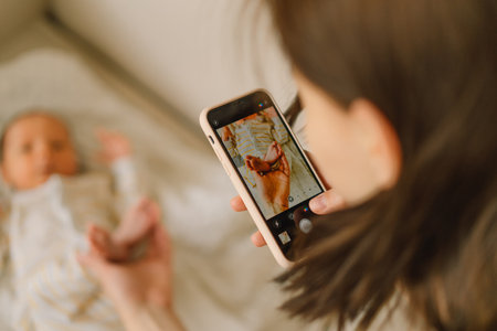 Mother taking photo of baby boy on mobile phone. Using technology