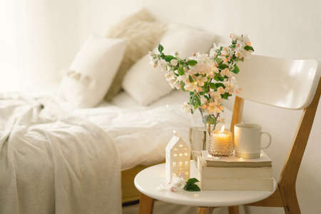Still life details in home interior of living room. Book, hot cup tea, candle and vase with apple spring flowers. Read and rest. Cozy spring concept.の写真素材