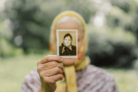 Old woman remembers her youth. Grandma keeps her photo in her youth. Memories. Vintage old photos