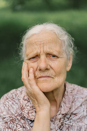 Portrait Sad old woman. Portrait of a gray-haired adult grandmother against the background of nature. Depressed elder suffering from lonelinessの写真素材