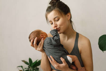 Mother holds and hugs her newborn baby son at home. Happy infant and mom.