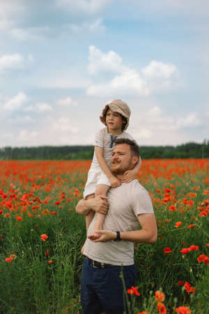 Happy fathers day. Little boy and father are playing in a beautiful field of red poppies.の写真素材