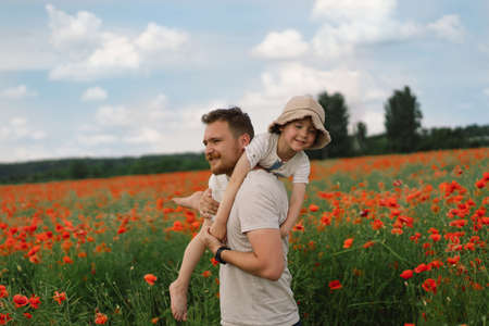 Happy fathers day. Little boy and father are playing in a beautiful field of red poppies.の写真素材