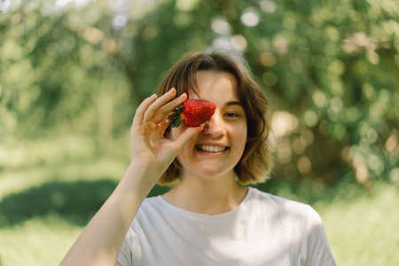 Young Teenager Girl with strawberry in a t-shirt in a outdoor and looking at camera. People and...