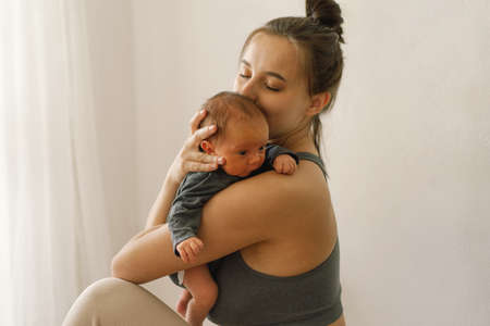 Mother holds and hugs her newborn baby son at home. Happy infant and mom.の写真素材