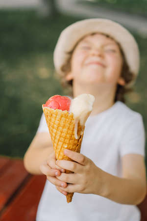 Boy in a hat is holding an ice cream and looks happy and surprised. Summer food and summer timeの写真素材