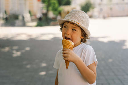 Boy in a hat is holding an ice cream and looks happy and surprised. Summer food and summer time