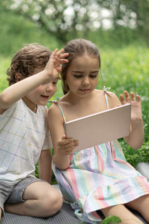 Children with a tablet outdoors. Kids speak by video call. Technology concept.の写真素材