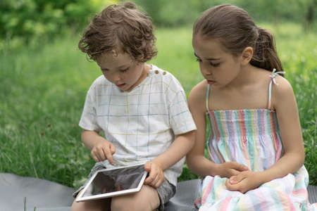 Children with a tablet outdoors. Children play games on the tablet. Technology concept.の写真素材