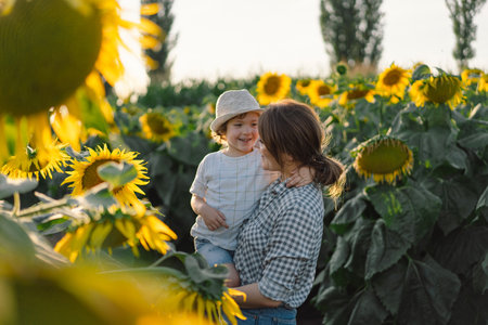 Mother with little baby son in sunflowers field during golden hour. Mom and son are active in natureの写真素材