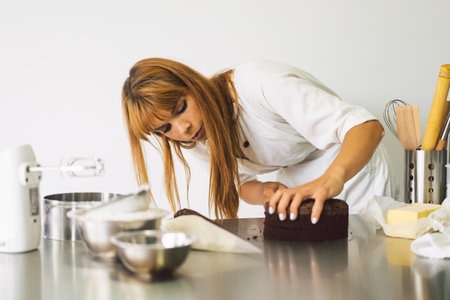 Confectioner girl is preparing a cake biscuit with white cream and chocolate. Cooking cakes.の写真素材