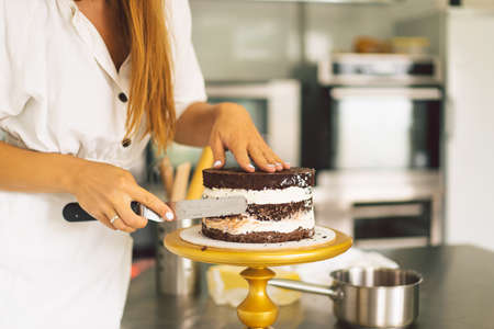 Confectioner girl is preparing a cake biscuit with white cream and chocolate. Cooking cakes.