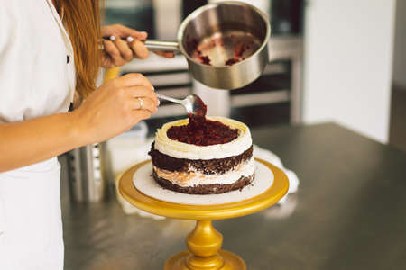 Confectioner girl is preparing a cake biscuit with white cream and chocolate. Cooking cakes.の写真素材