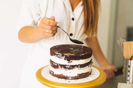 Confectioner girl is preparing a cake biscuit with white cream and chocolate. Cooking cakes.の写真素材