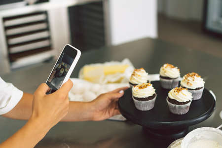 Confectioner girl photographing cupcake for her blog. Girl makes a photo of cupcakes on a smartphoneの写真素材