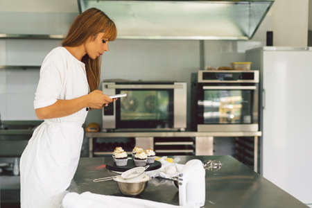 Confectioner girl photographing cupcake for her blog. Girl makes a photo of cupcakes on a smartphoneの写真素材