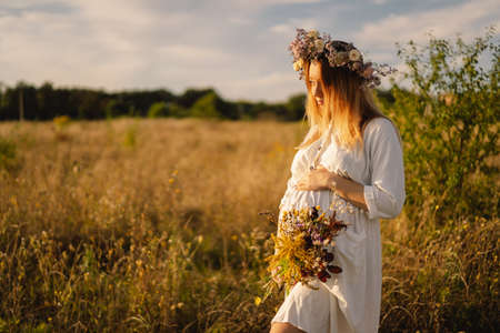 Portrait of a pregnant woman. A beautiful young pregnant woman in a white dress walks in the field.の写真素材