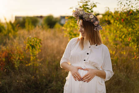 Portrait of a pregnant woman. A beautiful young pregnant woman in a white dress walks in the field.の写真素材