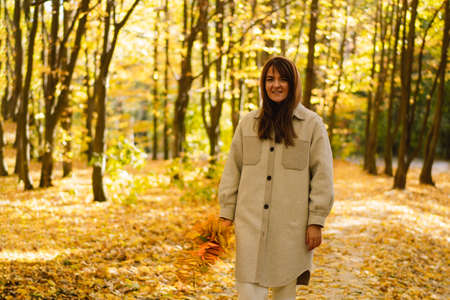 Woman in a long shirt with a bouquet of autumn leaves in her hands walks through the autumn forest.の写真素材