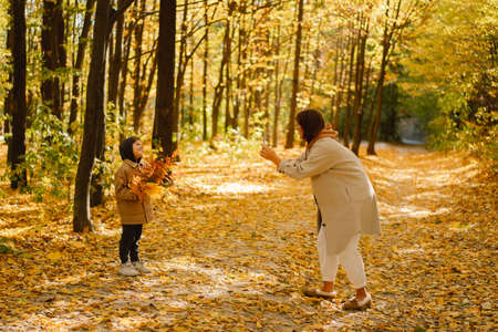 Mom and son take a selfie on the phone in the autumn forest. People use technology.