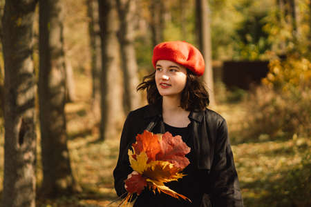 A Teengirl in a red beret with a bouquet of autumn leaves in her hands walks through the forestの写真素材