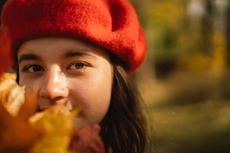 A Teengirl in a red beret with a bouquet of autumn leaves in her hands walks through the forest