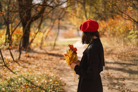 A Teengirl in a red beret with a bouquet of autumn leaves in her hands walks through the forestの写真素材