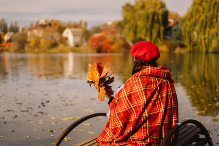 A Teengirl in a red beret reading book on wooden pontoon. Autumn season.の写真素材