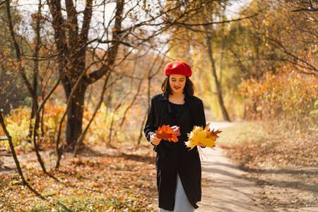 A Teengirl in a red beret with a bouquet of autumn leaves in her hands walks through the forestの写真素材