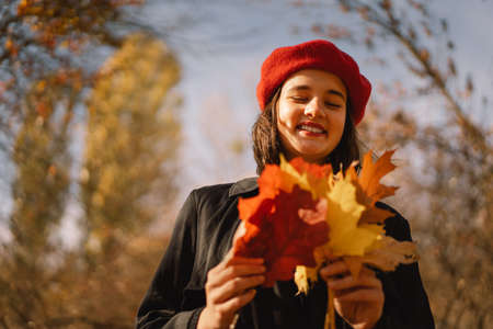 A Teengirl in a red beret with a bouquet of autumn leaves in her hands walks through the forest