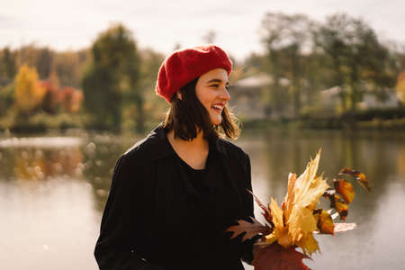 A Teengirl in a red beret with a bouquet of autumn leaves in her hands walks through the forestの写真素材