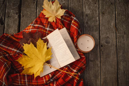 Open book with candle and bouquet of autumn leaves with a plaid on a wooden backgroundの写真素材
