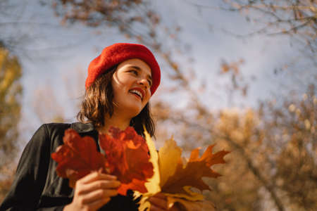 A Teengirl in a red beret with a bouquet of autumn leaves in her hands walks through the forestの写真素材
