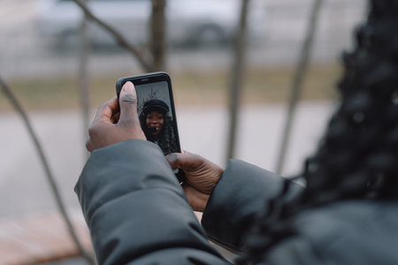 Afro girl takes a selfie on the phone on the outdoors. People using technologyの写真素材